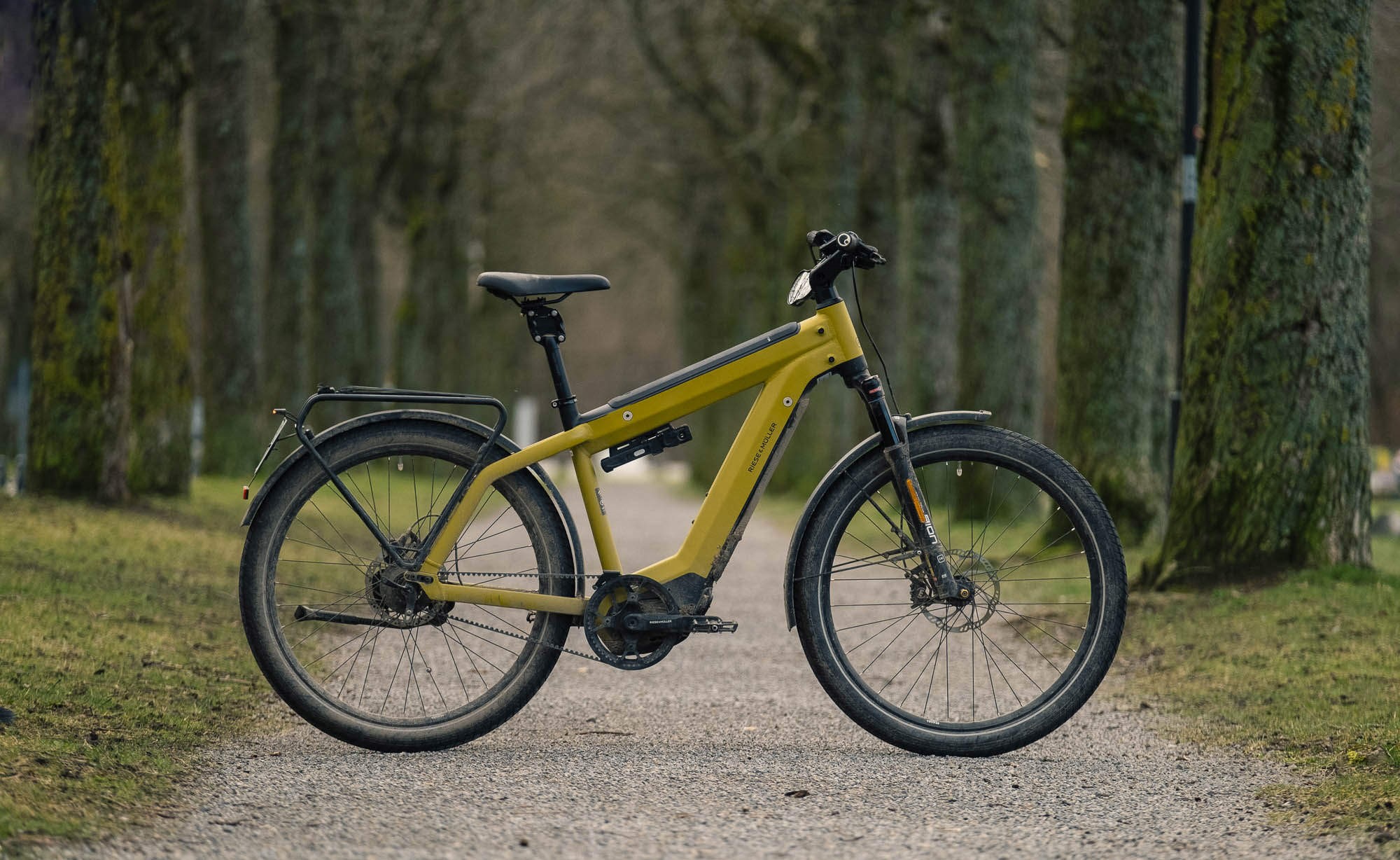 yellow and black riese muller ebike is standing on a rough road between the trees