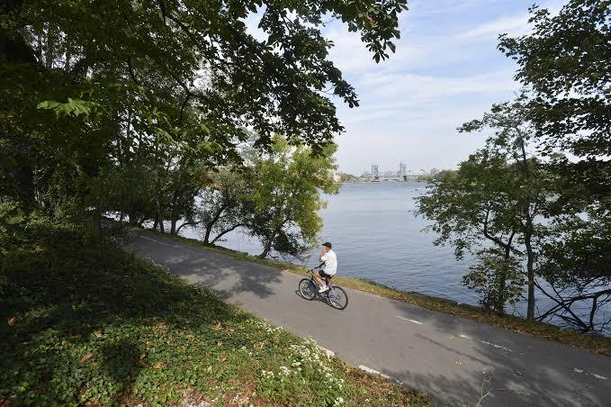A man with white shirt is riding an ebike on a road of Randall's Island