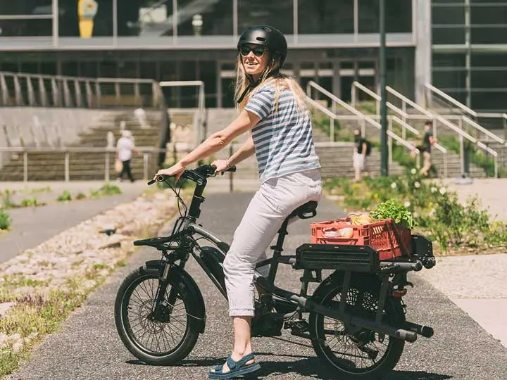 A woman riding a electric bike with a basket on the back.