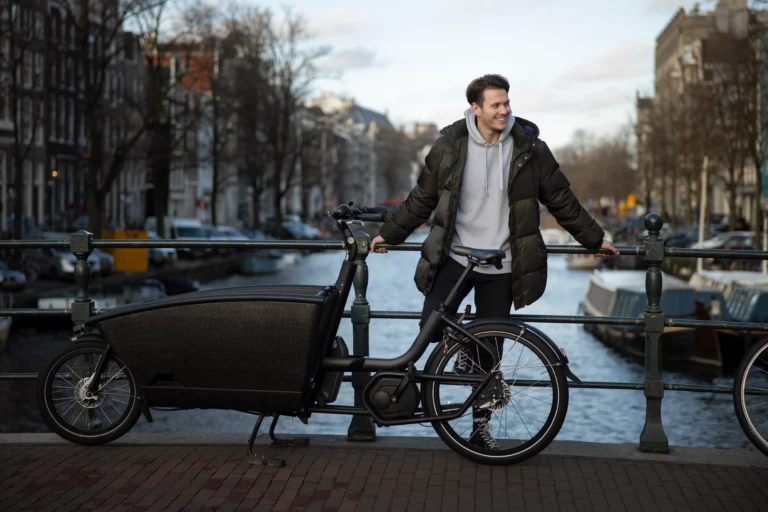 A man standing next to a electric cargo bike on a bridge.