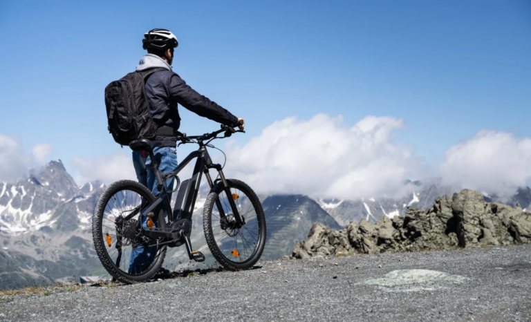 Cyclist standing with an electric bike on a mountain trail, highlighting “Why Ebikes Are a Better Choice for the Environment” through eco-friendly, zero-emission outdoor travel.